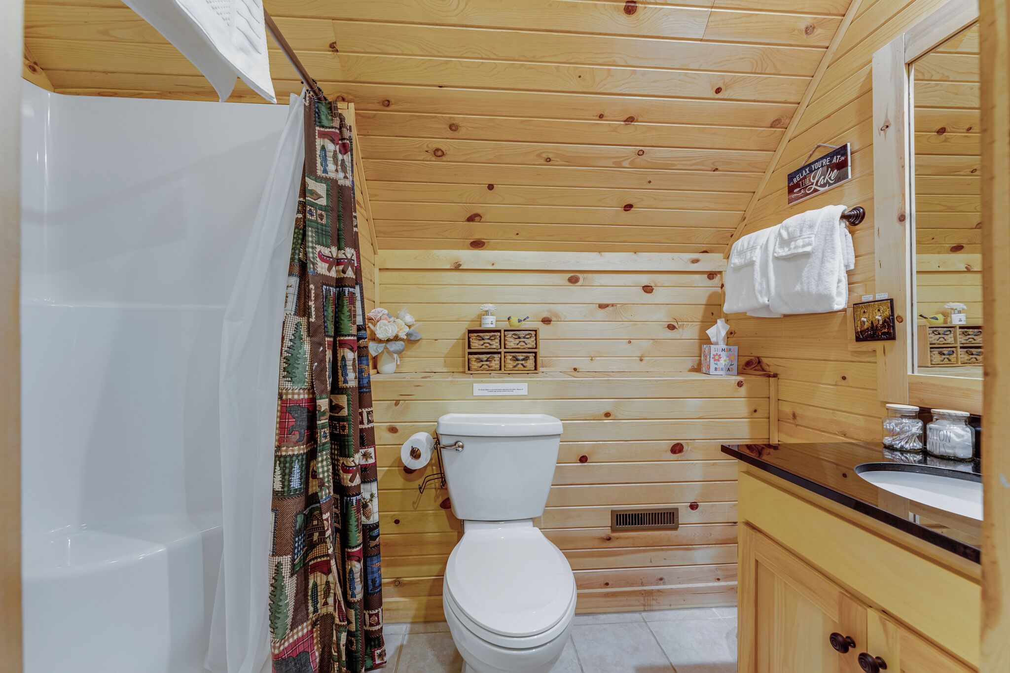 A wooden cabin bathroom with a toilet, sink, and shower.