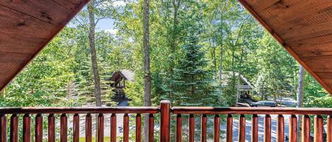 A wooden deck with a view of a forest and a cabin.
