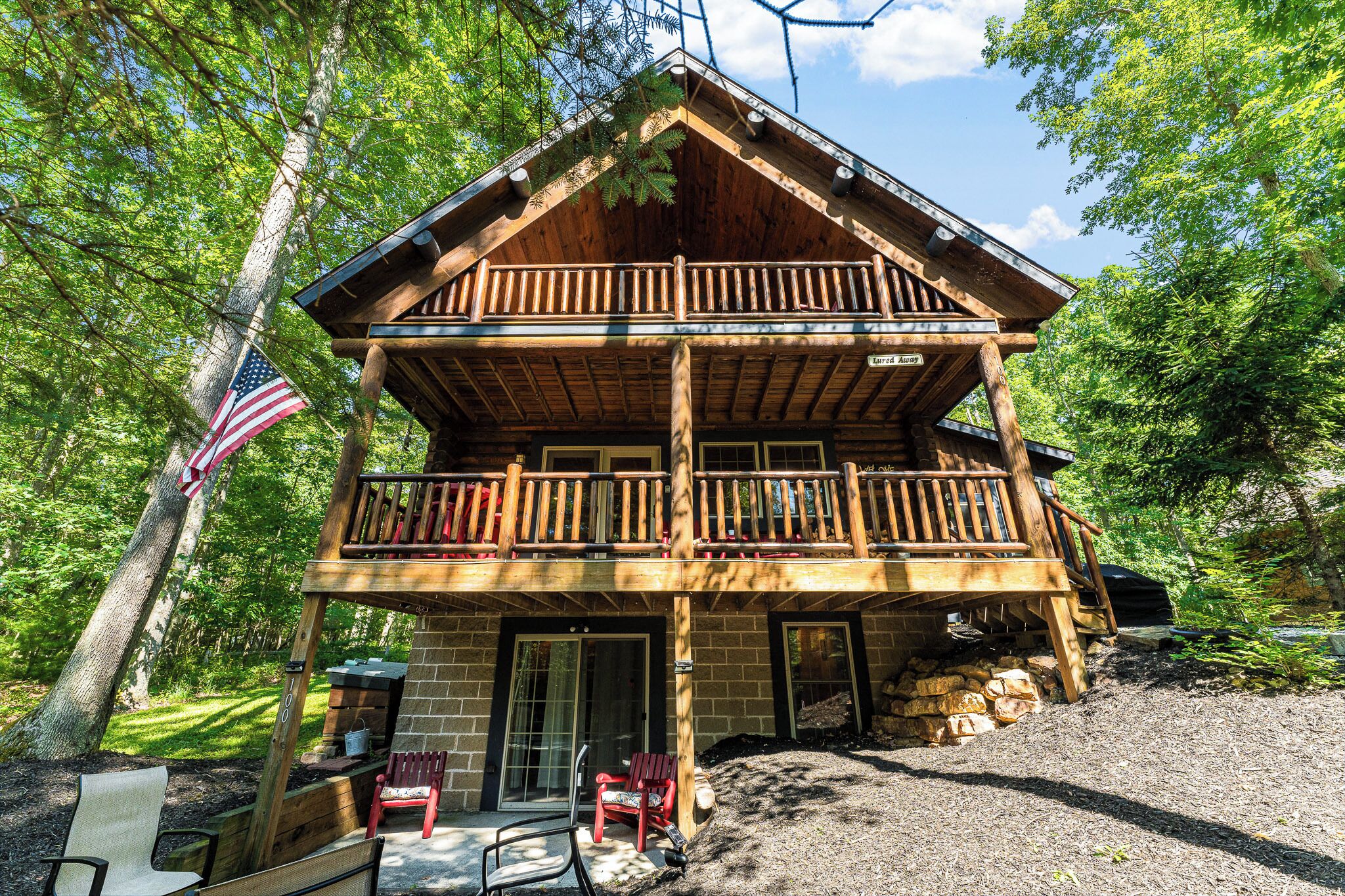 A two-story log cabin with a balcony, a flag, and outdoor seating.