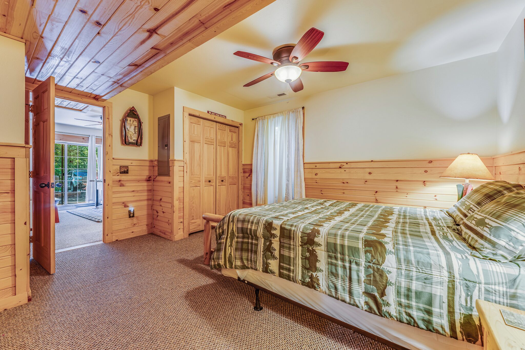 Ein Schlafzimmer mit Holzwandverkleidung, einem Bett, einem Deckenventilator und einer Tür zu einem Außenbereich.