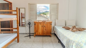 Una habitación con literas, un armario de madera, un ventilador de pie y una cama con una toalla.