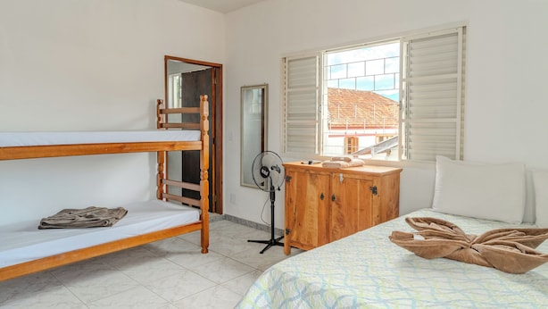 Una habitación con una cama litera, un aparador de madera, un ventilador y una ventana con persianas.