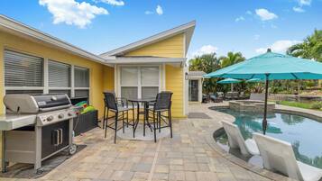 A patio area with a grill, outdoor seating, and a swimming pool.