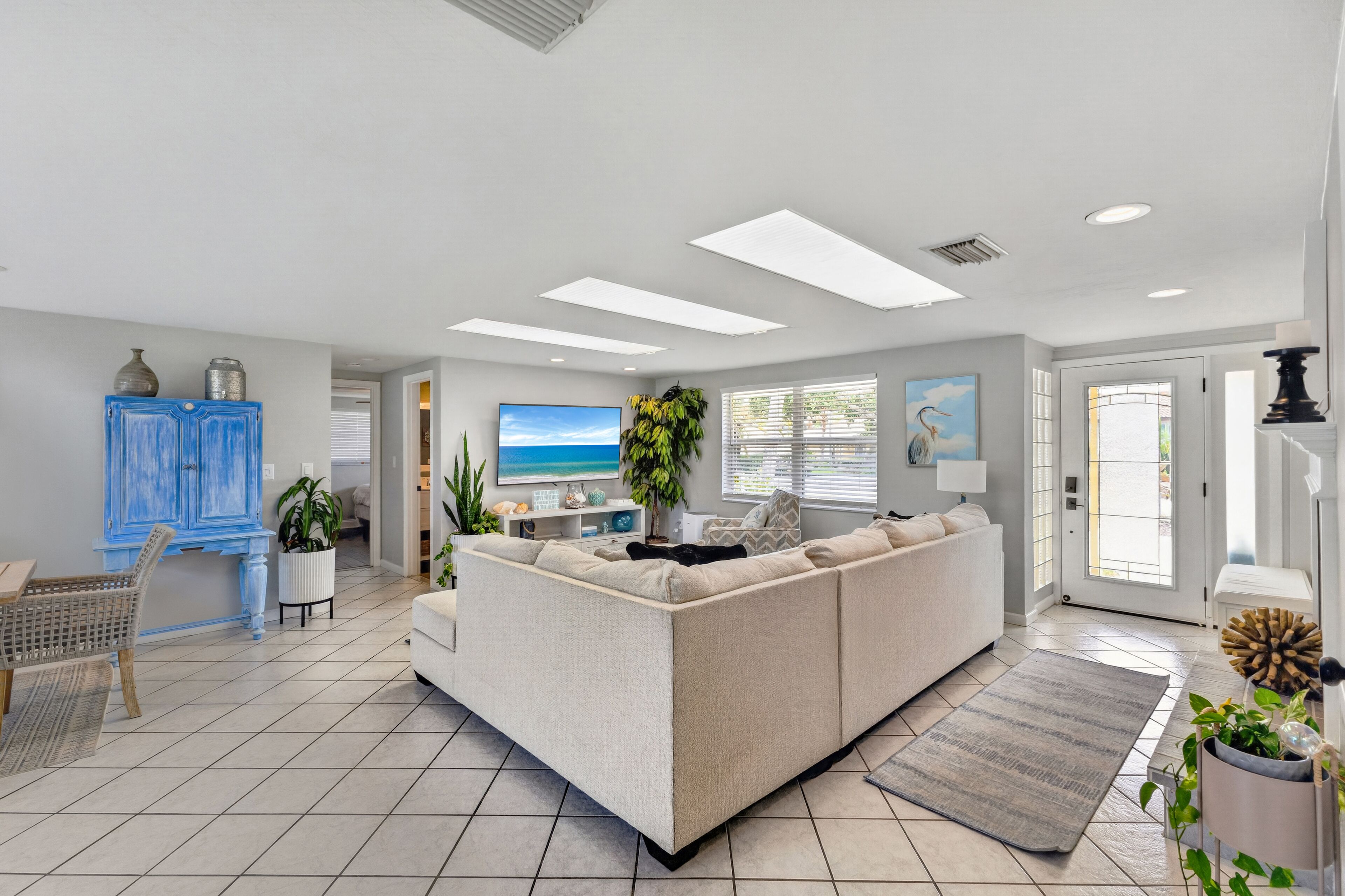 A modern living room with a sectional sofa, a dining area, and a view of the outdoors through large windows.