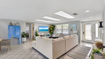 A modern living room with a sectional sofa, a dining area, and a view of the outdoors through large windows.