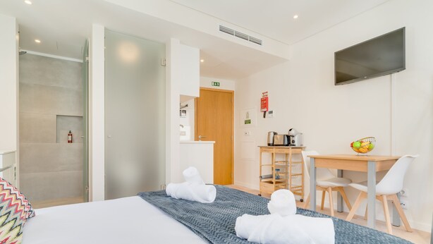 Ein Hotelzimmer mit Bett, Schreibtisch und Stuhl. Ein Duschbereich ist durch eine offene Tür sichtbar.