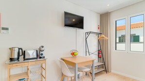 Ein modernes Zimmer mit einem Holztisch, weißen Stühlen, einem an der Wand montierten Fernseher und einem Fenster mit Blick auf Gebäude.