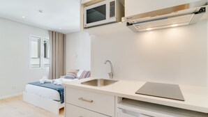 Ein modernes Hotelzimmer mit einem Bett, einer eingebauten Mikrowelle, einem Waschbecken und einem Laptop auf der Arbeitsfläche.