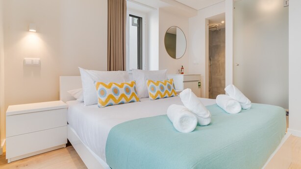 Habitación de hotel moderna con una cama bien tendida, una mesita de noche, un baño con ducha y un espejo grande.