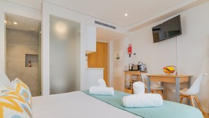 Habitación de hotel con cama, escritorio y silla, televisión y una pequeña mesa con frutero.