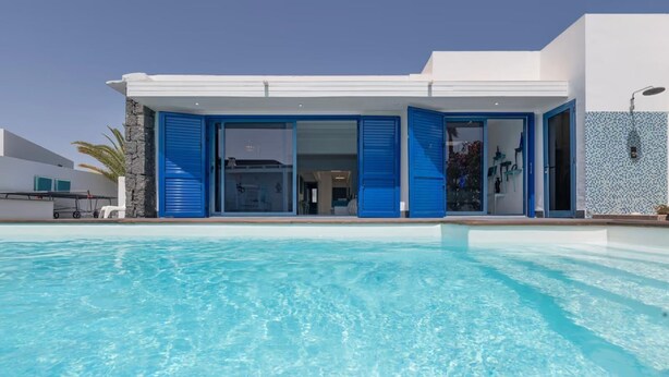 A modern building with a pool in front, featuring large glass doors and blue shutters. - Villa LunaMoon (Playa Blanca)