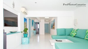 A modern living room with a teal sofa, a coffee table, and a TV. There are potted plants and artwork on the walls. - Villa LunaMoon (Playa Blanca)