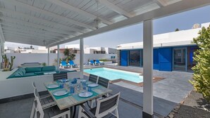 An outdoor pool area with a covered patio, seating, and a dining setup. - Villa LunaMoon (Playa Blanca)