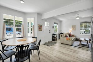 A spacious living area with a round wooden table and black chairs, a beige sofa, and a white ceiling fan.