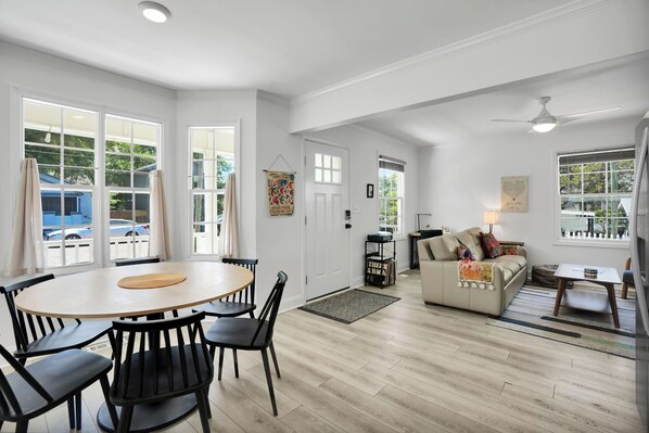 A spacious living area with a round wooden table and black chairs, a beige sofa, and a white ceiling fan. - Yellow Swann - Cozy Cottage Minutes from Live Oak Pavilion! (Wilmington)