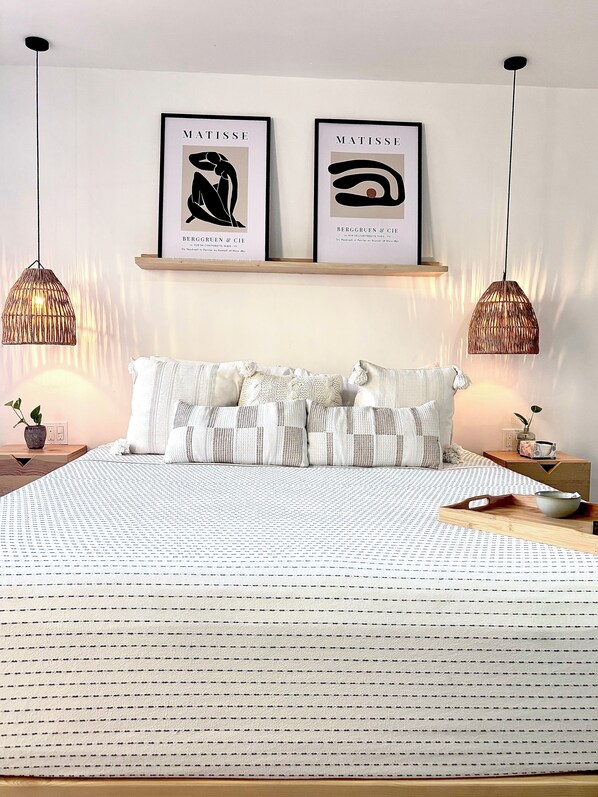 Une chambre à coucher avec un lit, deux lampes fixées au mur et deux œuvres d’art encadrées au-dessus du lit.