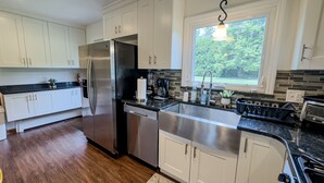 A modern kitchen with white cabinets, stainless steel appliances, and a large window providing a view of the outdoors. - Elegant 4BR Princeton Escape • Game Rm • Big Yard (Princeton)
