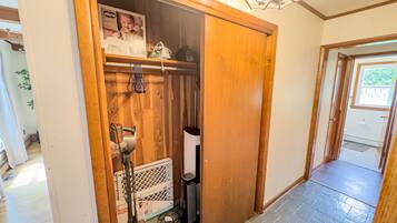 A wooden closet with a baby seat, a vacuum cleaner, and a trash can.