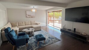 A modern living room with a beige sectional sofa, a blue armchair, a coffee table, and a flat-screen TV mounted on the wall. - Coastal 3 Bedroom, heated pool, walk to the beach and restaurants (Cocoa Beach)