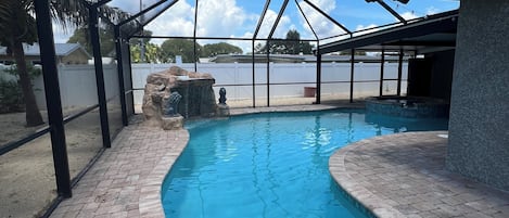 A swimming pool with a stone border and a covered area with metal beams.