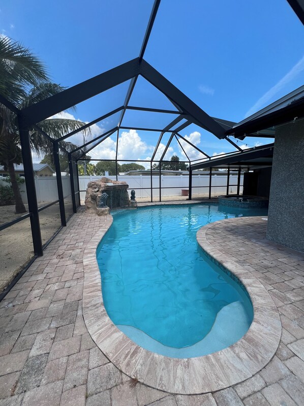 A swimming pool with a stone border and a covered area with metal beams.