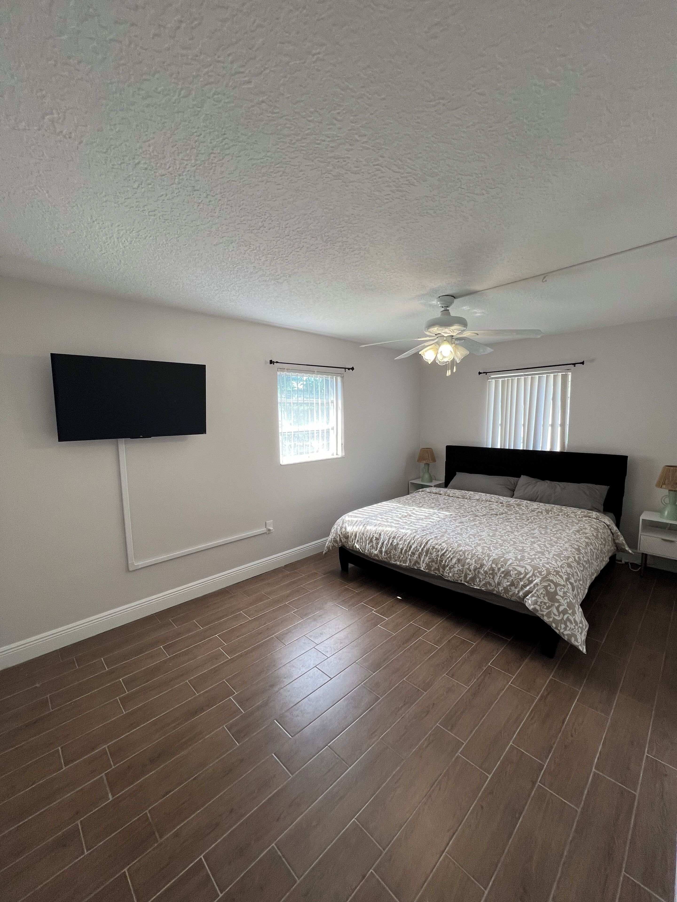 A bedroom with a bed, a ceiling fan, and a TV mounted on the wall.