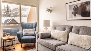 En hyggelig stue med en blå lænestol, en grå sofa og et lille træbord. Et indrammet billede af en bison er på væggen, og en lampe står på et sengebord.