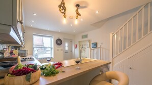 A kitchen with a wooden countertop, a fruit bowl, a wine glass, and a clock on the wall.