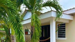 A building with a covered porch, palm trees, and a window with horizontal blinds.