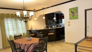 A dining area with a table set for four, a chandelier, and a kitchen in the background.