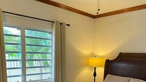 A bedroom with a bed, a ceiling fan, a window with curtains, and a bedside lamp.