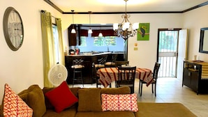 A living room with a sectional sofa, dining area, kitchen, and a view of the outdoors.