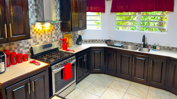 A kitchen with dark wooden cabinets, a stainless steel sink, a stove, and a window with red curtains.