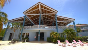Un edificio con un vestíbulo techado, palmeras y sillas de playa.