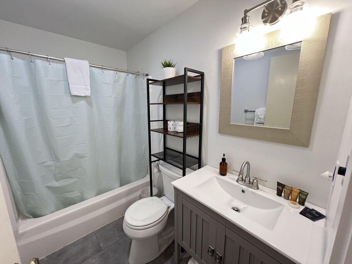 Une salle de bain équipée d’une baignoire, de toilettes et d’un meuble-lavabo avec un miroir et des étagères.