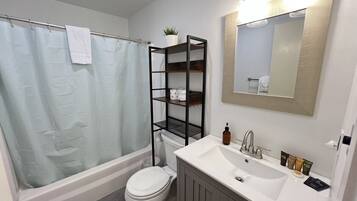 Une salle de bain équipée d’une baignoire, de toilettes et d’un meuble-lavabo avec un miroir et des étagères.