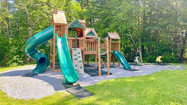 Ein Spielplatz mit Rutschen und Klettergerüsten, umgeben von Bäumen.