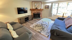 Ein Wohnzimmer mit Kamin, Sofas, einem Fernseher und einem gemusterten Teppich.