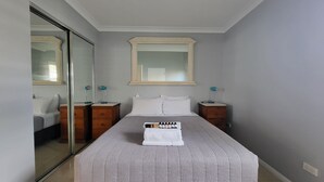 Ein Schlafzimmer mit einem Bett, zwei Nachttischen, einem Spiegel und einem Fenster.