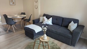 Un salon avec un canapé gris foncé, deux fauteuils assortis, une table basse ronde en verre et une petite table d’appoint sur laquelle est posé un vase.