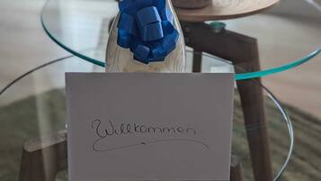 Une bouteille ornée d’un ruban bleu, posée sur une table en verre, à côté d’une pancarte indiquant « Bienvenue ».