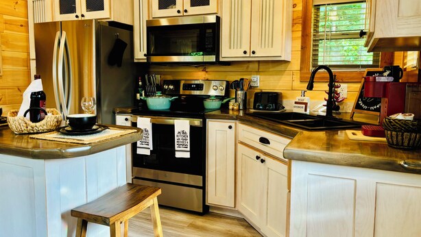 A compact kitchen with wooden cabinets, stainless steel appliances, and a small island with a stool. - Falcons Nest cabin with AC and WiFi in enchanting Calhoun TN (Calhoun)