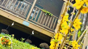 A wooden cabin with a balcony, surrounded by greenery and flowers. - Falcons Nest cabin with AC and WiFi in enchanting Calhoun TN (Calhoun)