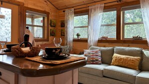 A cozy cabin interior with a wooden interior, a kitchen area with a counter, a dining table, and a sofa with cushions. - Falcons Nest cabin with AC and WiFi in enchanting Calhoun TN (Calhoun)