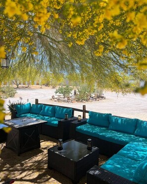 An outdoor seating area with a sectional sofa and a table, surrounded by greenery and a view of the beach. - Room 1 • Family Suite - Downtown Joshua Tree (Joshua Tree)