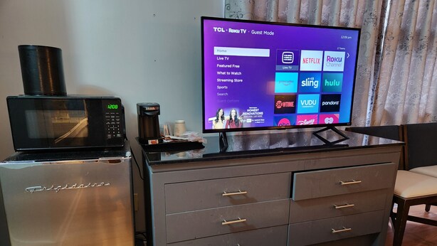 Une chambre d’hôtel équipée d’un téléviseur à écran plat affichant l’interface d’un service de diffusion en continu, d’un four à micro-ondes, d’une machine à café et d’un mini-réfrigérateur.