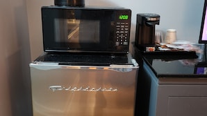 Une petite cuisine équipée avec un réfrigérateur en acier inoxydable, un micro-ondes noir et une machine à café posée sur le plan de travail.