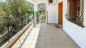 Ein Balkon mit Metallgeländer, Blick auf Bäume und Hügel, und ein gefliester Boden.