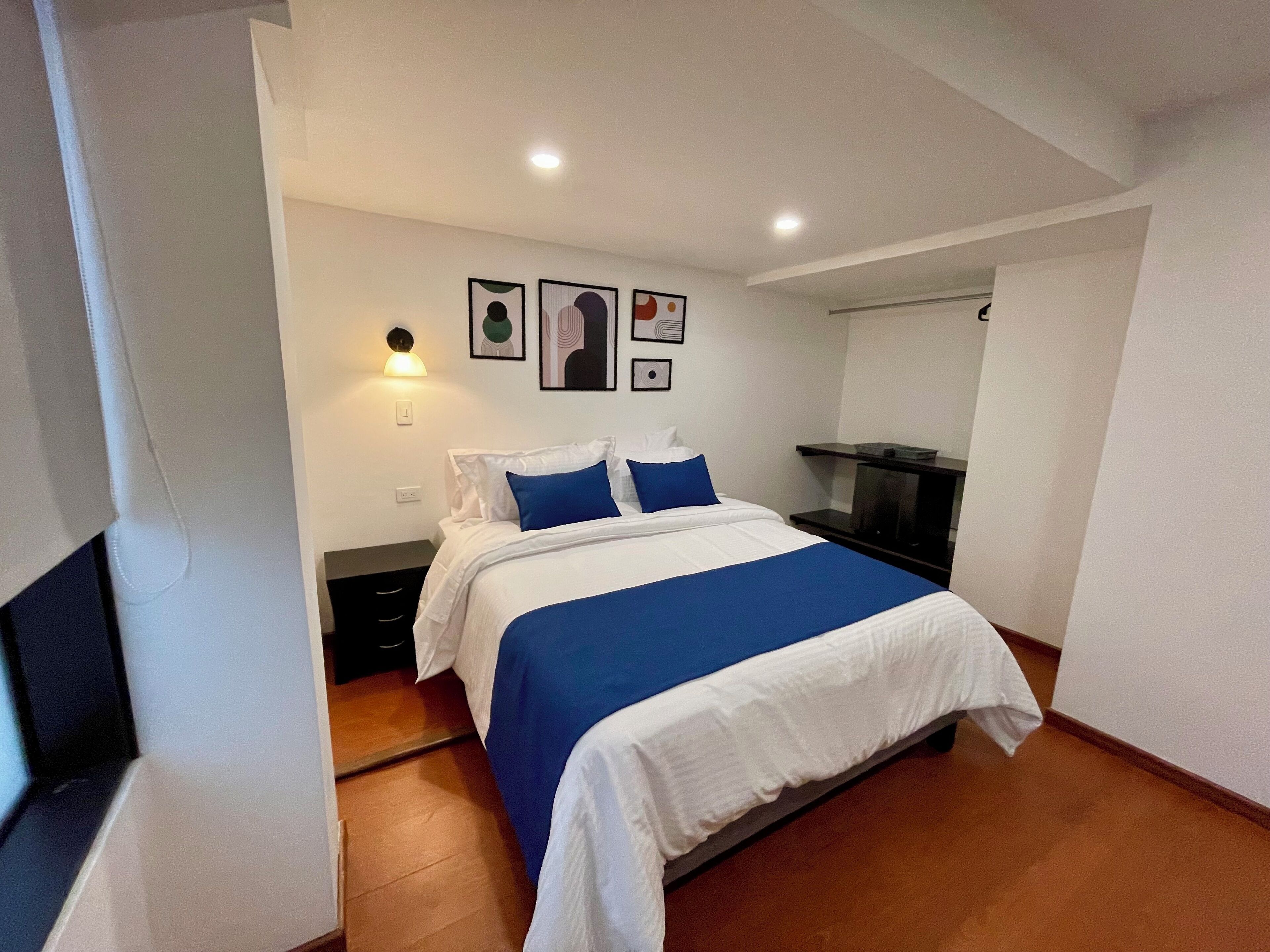 A hotel room with a bed, a nightstand, a desk, and a wall-mounted light.