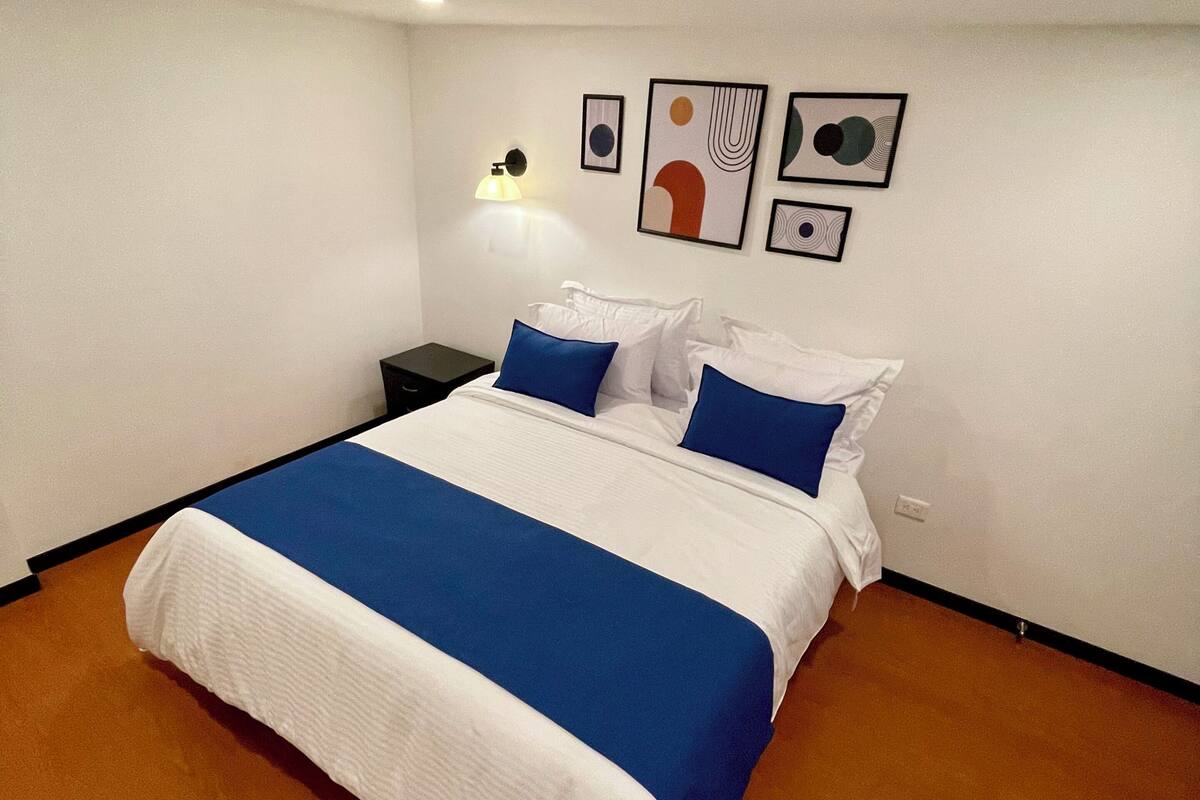 Ein Schlafzimmer mit einem Bett, einem Nachttisch, einer Wandlampe und abstrakter Kunst an der Wand.